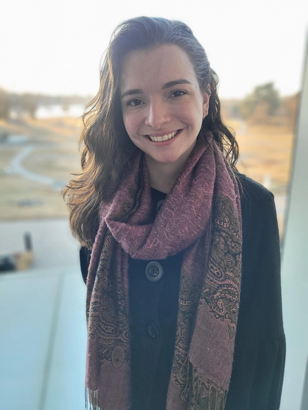 Caroline Boehm, smiling, in a mauve paisley scarf, by a sunlit window