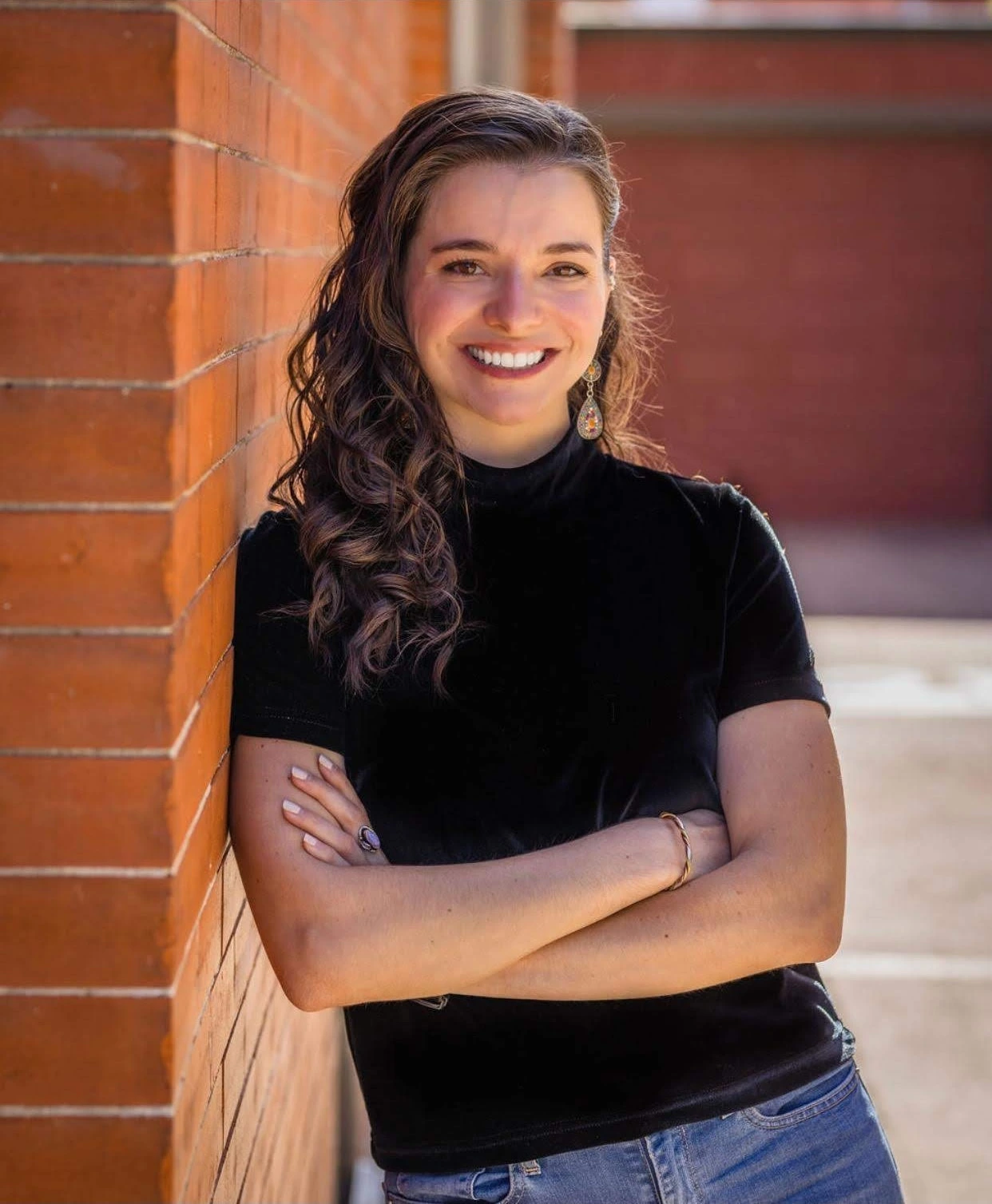 Caroline Boehm, smiling, arms crossed, leaning against a brick wall